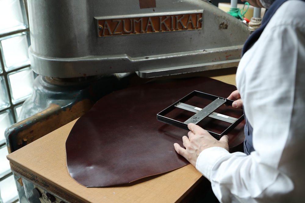 裁断機の前で茶色の革に抜き型を合わせる職人